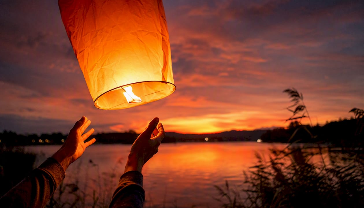 Hands releasing glowing paper lantern at dusk