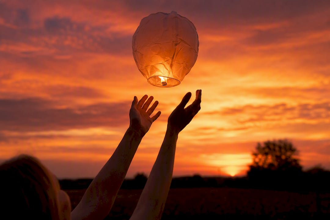 Hands releasing paper balloon at sunset outdoors
