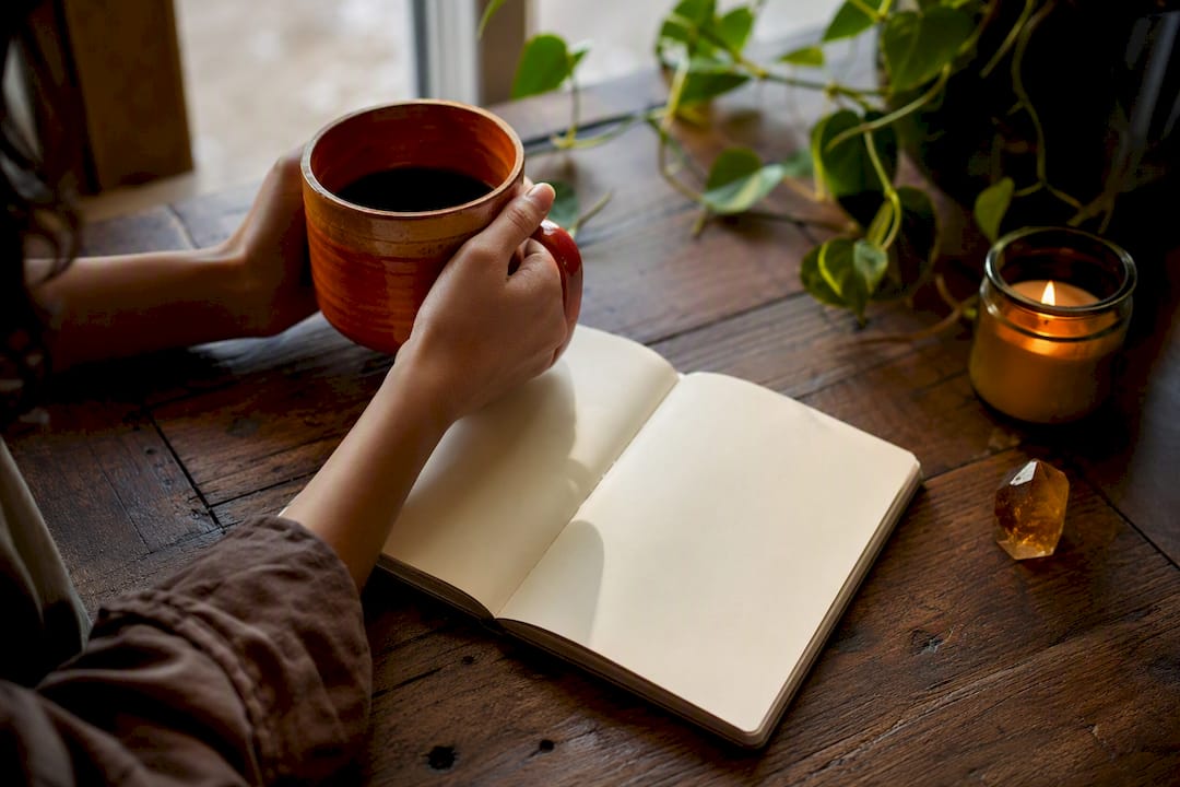 Hands holding mug next to journal in morning light