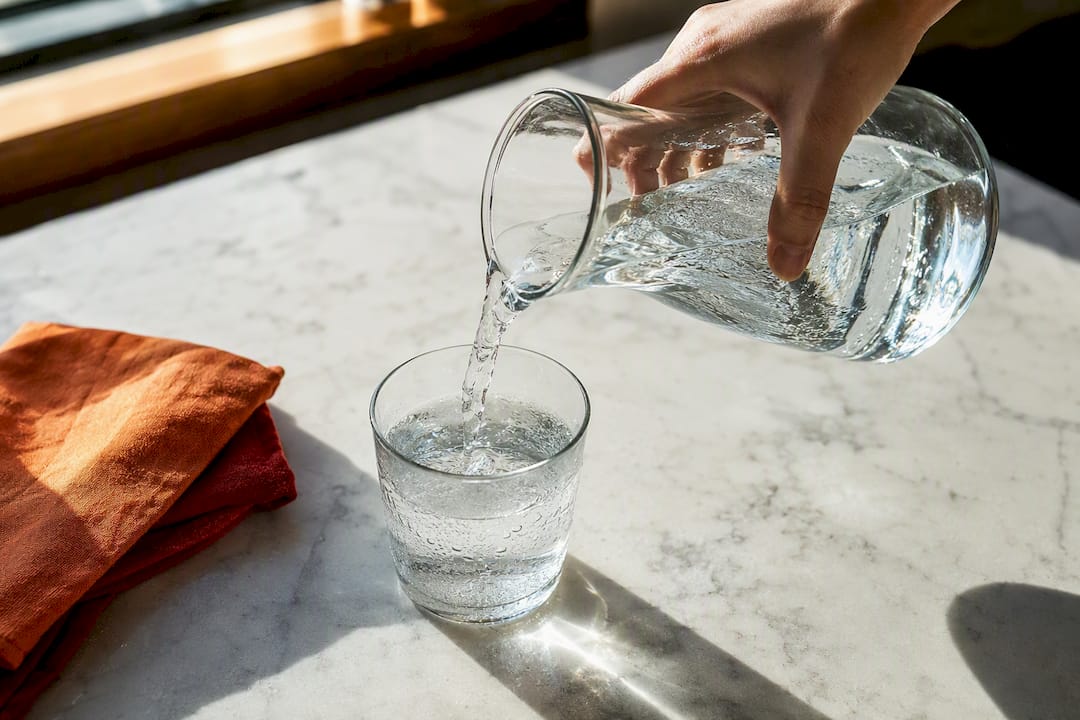 Hand pouring water into a clear tumbler